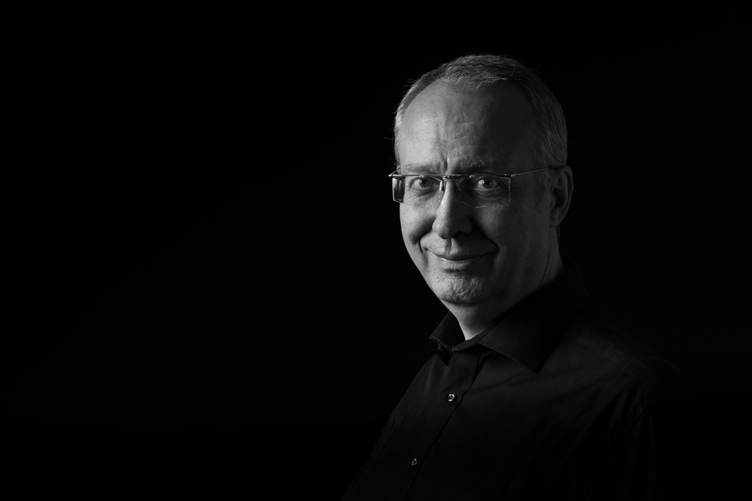 Artistic black and white portrait of an elderly man with glasses against a dark background.
